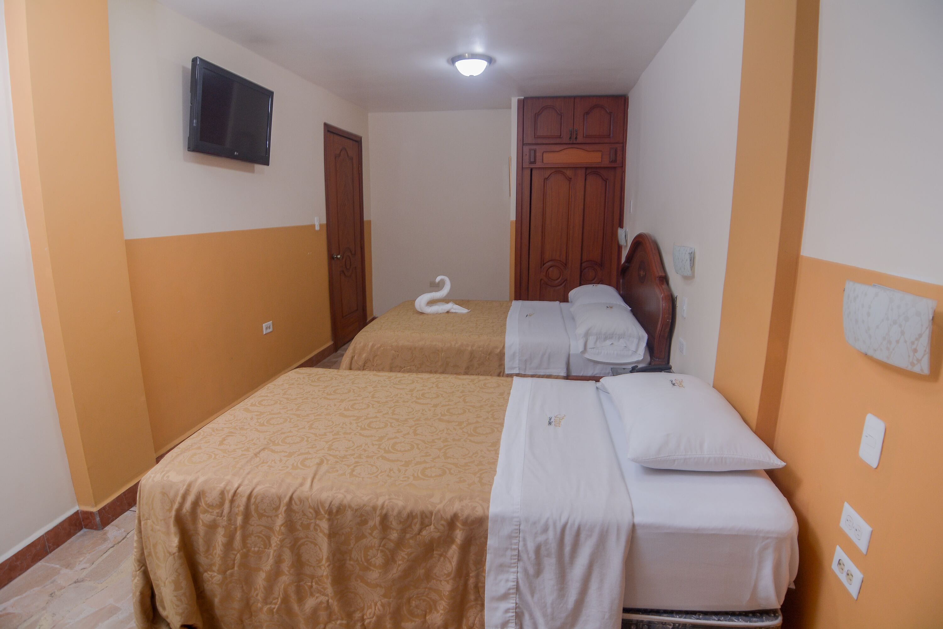 A hotel room with two beds, a television mounted on the wall, and a wooden wardrobe.