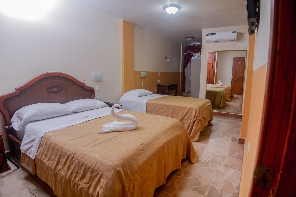 Habitación de hotel con dos camas, cada una con una almohada con forma de cisne, una mesita y un equipo de aire acondicionado montado en la pared.