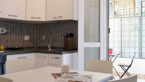Une cuisine moderne avec des meubles blancs, un pare-feu noir en carreaux et un coin repas comprenant une table et des chaises.