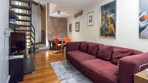 A living room with a sofa, a TV, a staircase, and a dining area. - GuestHost - Stylish Apt w/king size bed M1 Porta Venezia (Milan)