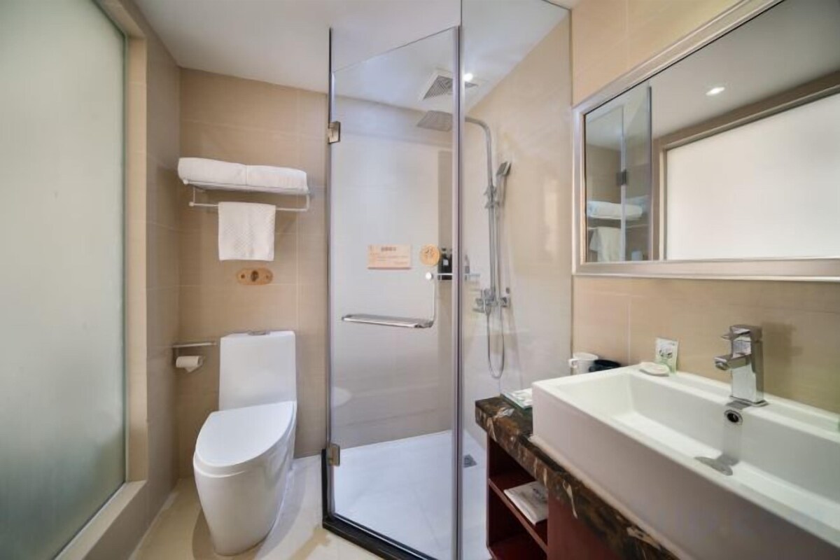 A modern bathroom with a glass shower enclosure, a white toilet, and a large sink with a mirror above.