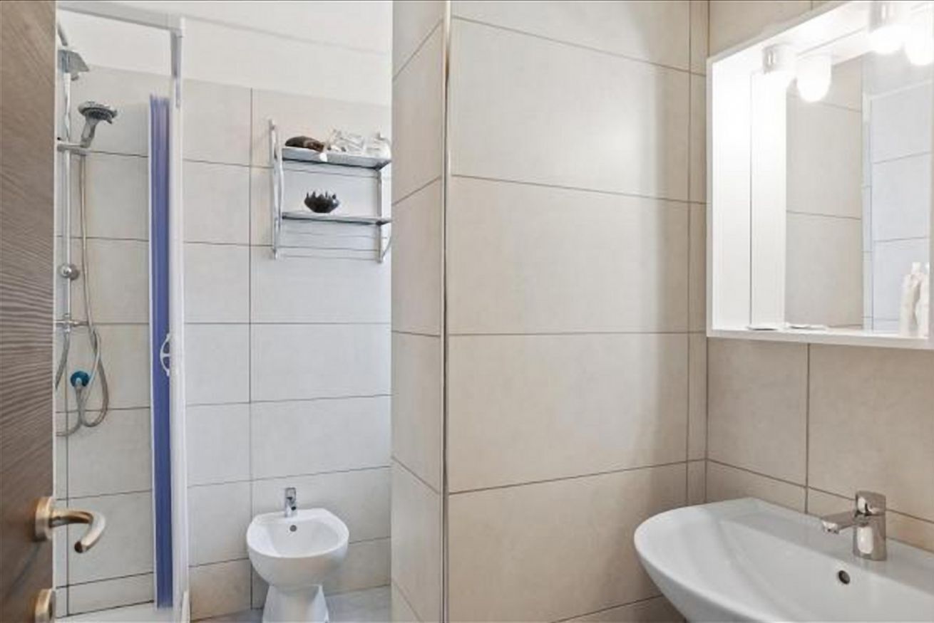 A bathroom with a shower, a bidet, a sink, and a mirror.