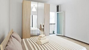 Une chambre à coucher comprenant un lit, une armoire, un miroir et une porte donnant sur un balcon.