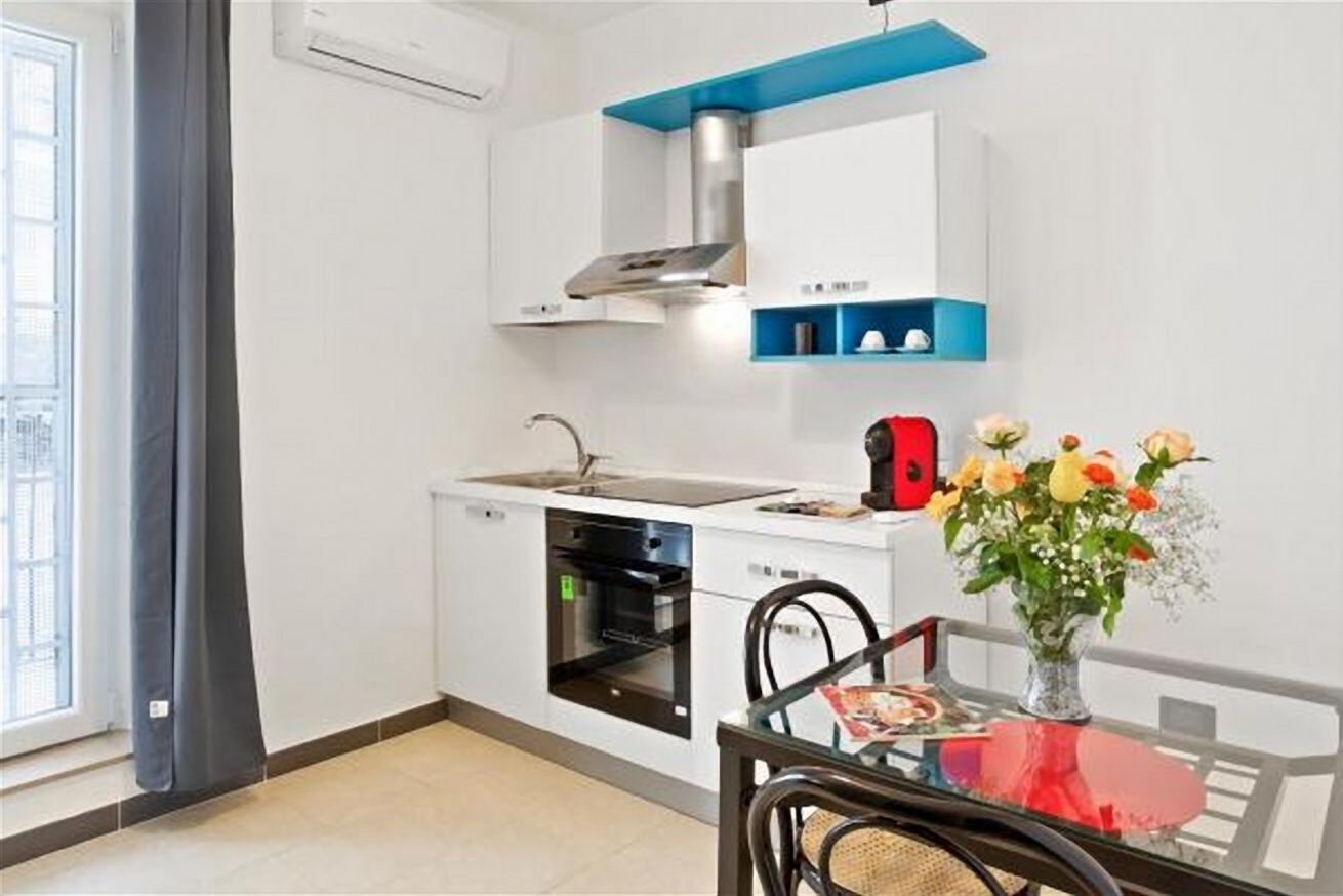 A compact kitchen with a built-in oven, a stainless steel range hood, and a small window.