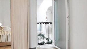 Une pièce avec un lit, une porte en bois et un balcon doté d’une rambarde en métal.