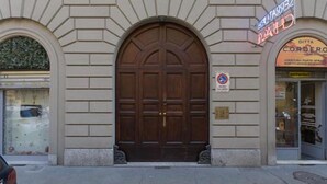 A building with a large wooden double door, a sign above the door, and a shop with a glass front to the right. - GuestHost - Cozy and stylish studio situated in the centre of Turin in a beautiful historical building with elevator. It is the ideal solution for both short business or leisure stays: the area has a good infrastructure and is well served by lots of faci (Turin)