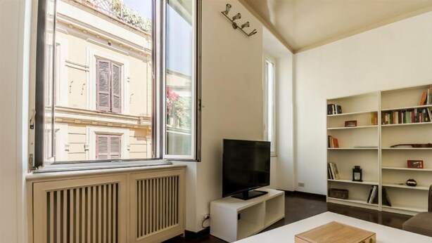 Un salon moderne doté d’une grande fenêtre, d’un téléviseur à écran plat, d’une bibliothèque et d’une table basse blanche.