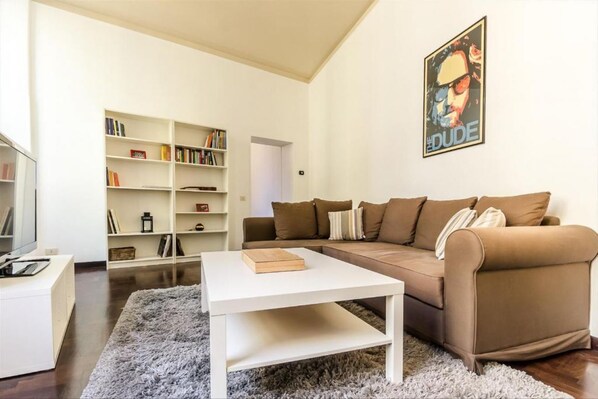 A living room with a brown sofa, white coffee table, and a bookshelf.