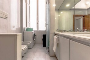 A compact bathroom with a toilet, washing machine, and sink.