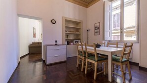 Un coin repas avec une table et des chaises blanches, un buffet en bois et une fenêtre avec des volets.
