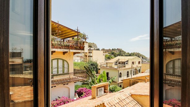 Un balcón con vistas a un pueblo, un pequeño jardín y un edificio con tejado de tejas.
