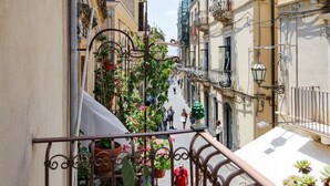 Una calle estrecha con balcones, macetas con plantas y gente caminando.