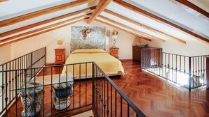 Un dormitorio en el ático con cama, vigas de madera, pared de piedra y una escalera.