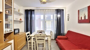 A room with a dining table, chairs, a red sofa, a ceiling fan, a TV, and a window with curtains. - GuestHost - Cozy two-room apartment - Piazza della Signoria! NEW (Firenze)