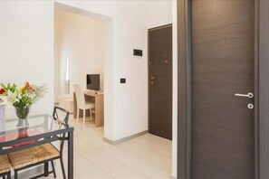 Une chambre d’hôtel moderne avec une table à manger en verre, un vase de fleurs, un bureau et une porte en bois foncé.