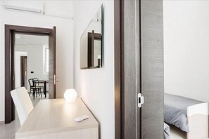Ein Hotelzimmer mit einem Bett, einem Nachttisch mit Lampe, einem Sessel, einem Schreibtisch und einem Spiegel an der Wand.
