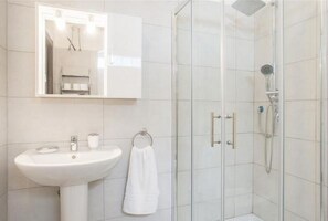 Ein Badezimmer mit weißem Waschbecken, einem Spiegel, einem Handtuchhalter und einer Duschkabine.
