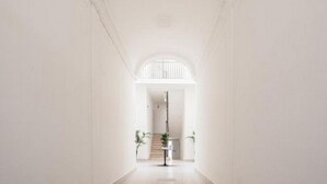 Een hal met een trap die uitkomt op een overloop, witte muren en een vloerlamp.