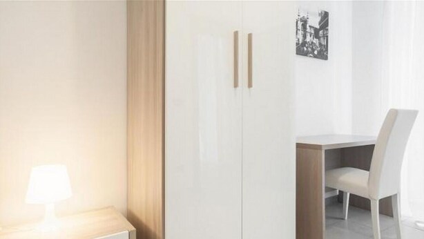 Een kamer met een bed, nachtkastje met lamp, kledingkast, bureau met stoel en een lijst aan de muur.