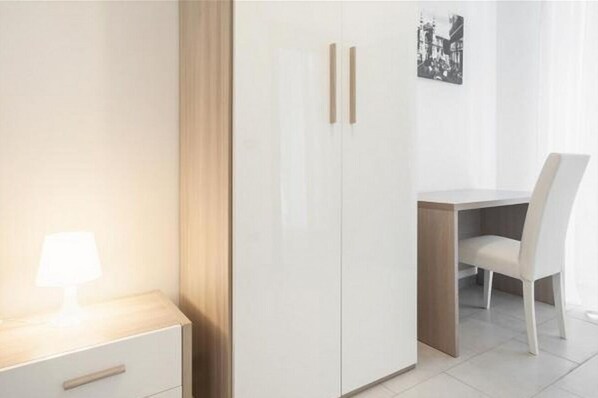Une chambre comprenant un lit, une table de chevet avec une lampe, une armoire, un bureau avec une chaise et un tableau encadré au mur.