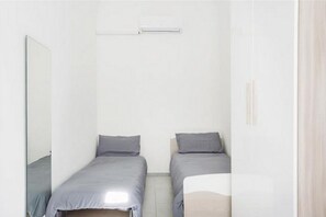 A small, single-room accommodation with two beds, a mirror, and a window.
