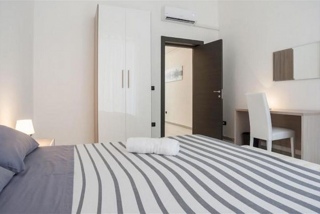 A hotel room with a bed, a desk, a chair, and a wardrobe.