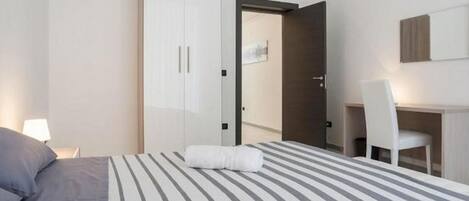 A hotel room with a bed, a desk, a chair, and a wardrobe.