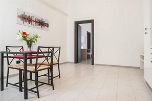 Un coin repas avec une table et des chaises, un vase rempli de fleurs et une œuvre d’art représentant un paysage urbain accrochée au mur.