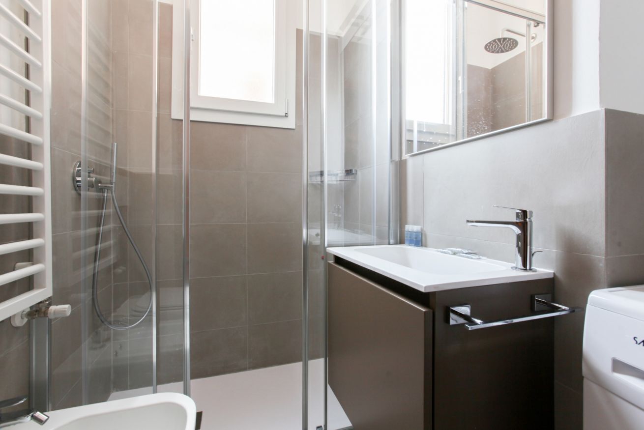 A modern bathroom with a glass-enclosed shower, a white sink, and a mirror.