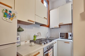 A compact kitchen with a gas stove, oven, microwave, and white cabinets. - GuestHost - NEW! Two-room apartment Tortona Design, Navigli, P.ta Genova (Milano)