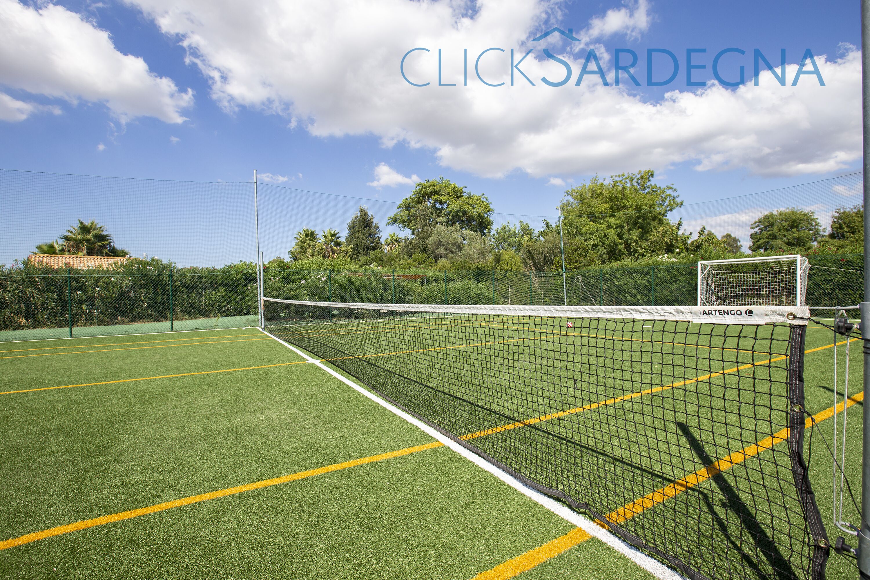 A tennis court with a net, goalpost, and surrounding fence.