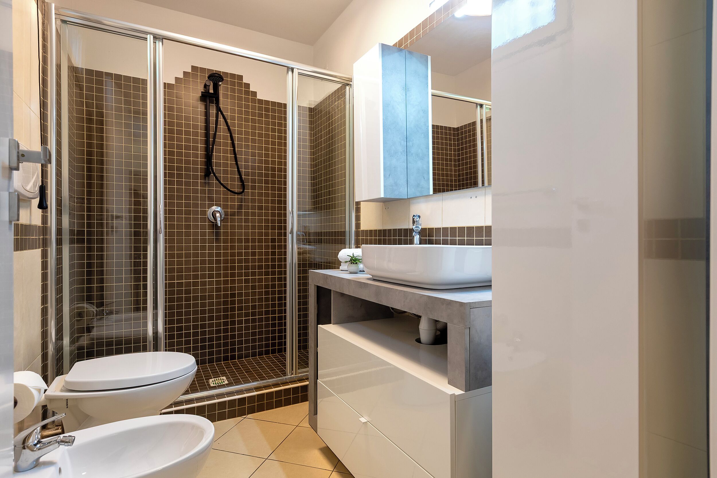 Ein modernes Badezimmer mit Duschkabine aus Glas, Toilette, Waschbecken und Waschtisch mit Spiegel.