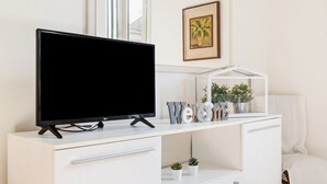 A white TV stand with a flat-screen TV, a framed picture, and a small plant on the shelf. - GuestHost - Casa Panigale Comfortable Apartment x4! NEW (Bologna)