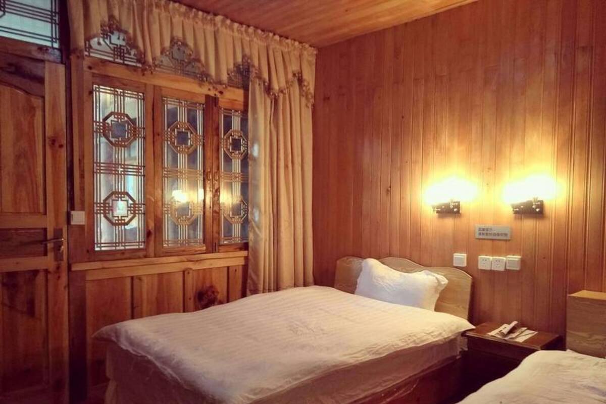 Ein Zimmer mit Holzwänden, einem Bett, einem Nachttisch und einem Fenster mit dekorativen Vorhängen.