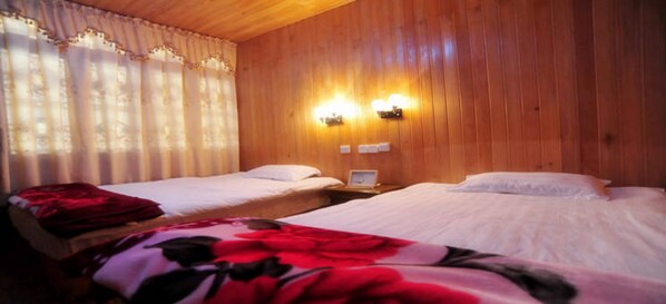 Una habitación con dos camas, paredes de madera y dos lámparas fijadas a la pared.