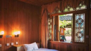 Une chambre traditionnelle en bois, avec un lit, deux lampes fixées au mur et une fenêtre donnant sur un paysage verdoyant.