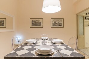 Ein Esstisch ist gedeckt mit Tellern, Gläsern und Besteck, darüber hängt eine Pendelleuchte und an der Wand befinden sich gerahmte Bilder.