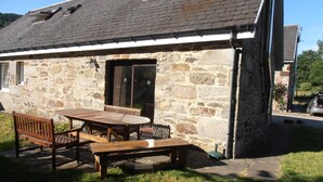 A stone building with a sloped roof, a wooden table and benches outside, and a clear sky. - Escape to Rural Highlands Stunning Scenery, Sound of the Burn  Licence PK11943F (Aberfeldy)