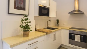 Una cuina moderna amb armaris blancs, una campana extractora d'acer inoxidable, un rentapeus i una tauleta amb una planta.