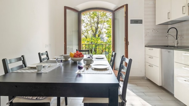 A dining area with a table set for four, a kitchen with white cabinets, and a view of trees through an open door. - GuestHost - Large, bright and well-kept apartment on the third floor of a building near the Maggiore Hospital. The historic center is easily accessible by public transport.The apartment, ideal for 5 people, is fully equipped and has 24h WiFi, A / C and h (Bologna)