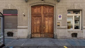 Una puerta doble de madera grande con un letrero encima, un escaparate y un persiano cerrado a la izquierda.