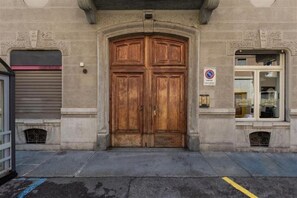 Une grande porte à double battant en bois, avec une enseigne au-dessus, une vitrine et un volet fermé sur le côté gauche.