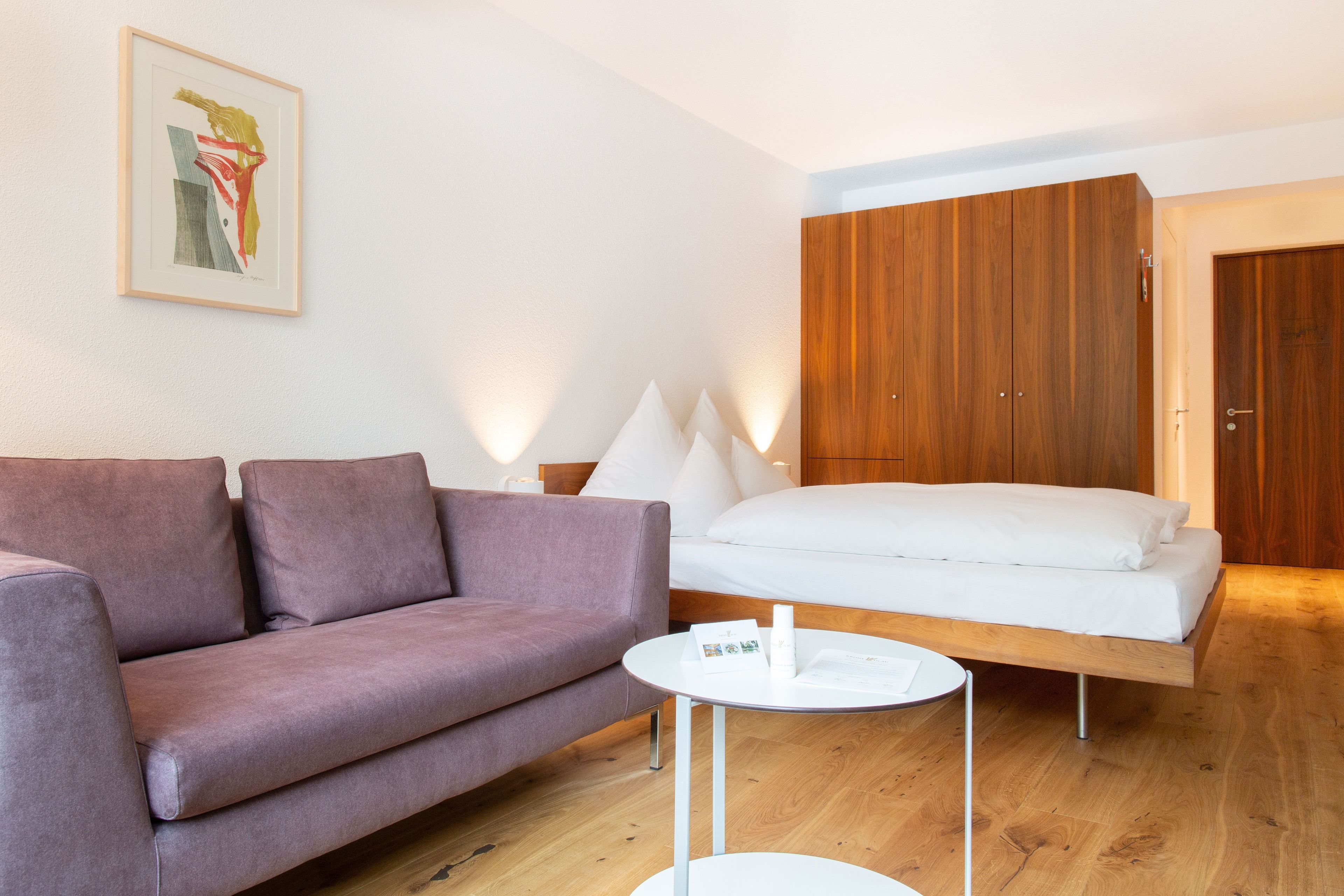 Ein modernes Zimmer mit einer Couch, einem Bett, einem Holzschrank und einem kleinen runden Tisch.