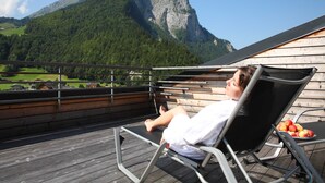 A person relaxing on a deck chair with a mountain view, a wooden deck, and a plate of apples.