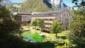 A modern hotel with a pool, surrounded by lush greenery and mountains.