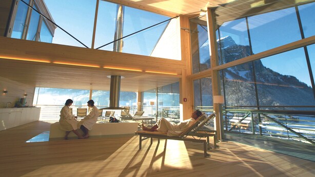 A spacious room with large windows, a wooden ceiling, and a view of mountains.