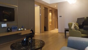 A modern living room with a flat-screen TV, a coffee table, and a sofa. There is a wooden cabinet with a water dispenser and a remote control. - Manhattan Langde Apartment (Guangzhou)