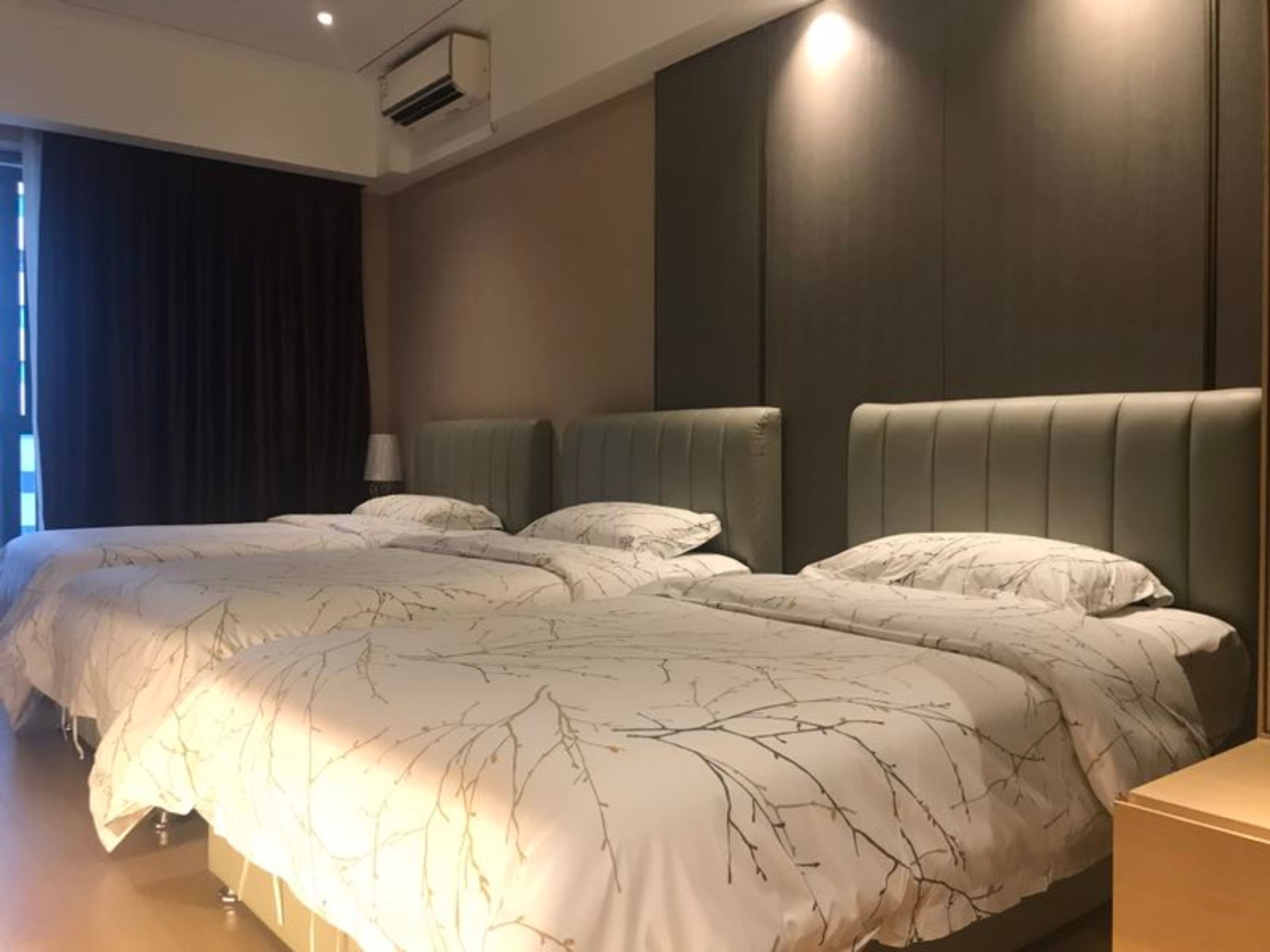 A modern hotel room with two beds, a large window with curtains, and a wall-mounted air conditioner.