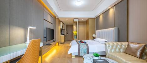 A modern hotel room with a bed, a sofa, a dining table, and a TV.