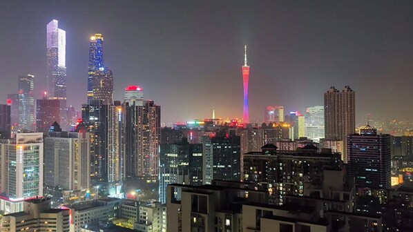 Paisagem urbana noturna com arranha-céus iluminados, incluindo uma torre imponente com um pináculo.